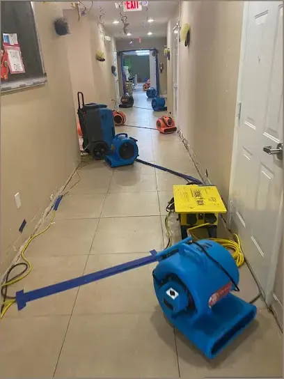 Air movers and a dehumidifier drying a long tiled hallway after a leak