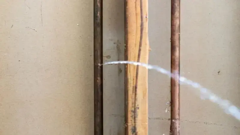 Thin jet of water spraying from a pinhole in a copper supply pipe inside an open wall, Laguna Niguel pinhole leak